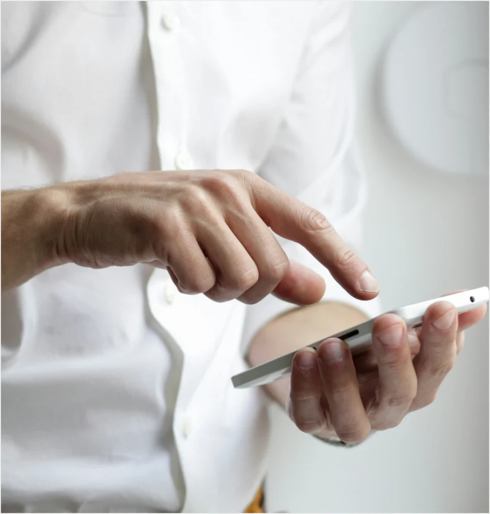 Close-up of hands holding and interacting with a white smartphone against a blurred light background.